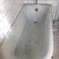 An old, worn, white bathtub with a gray, stained bottom in a bathroom with white subway tile walls.