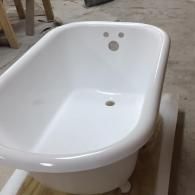 A white, freestanding clawfoot bathtub with a faucet and drain hole, shown in an unfinished workshop setting.