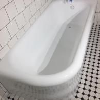 A white porcelain bathtub set against white subway tile walls and a black-and-white penny tile floor.