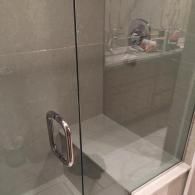 A glass shower door with a polished chrome handle, revealing a tiled bench seat and shower fixtures inside.