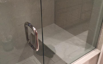 A glass shower door with a chrome handle, opening to a tiled built-in seat inside a modern shower enclosure.