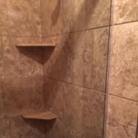 A shower wall tiled in brown, textured stone with two built-in corner shelves.