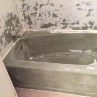 A bathtub in a bathroom undergoing renovation, with walls covered in grey joint compound and a faucet visible on the left.