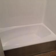 A clean, empty white bathtub installed against a plain white wall in a bathroom.