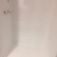 A white, empty walk-in shower stall with chrome fixtures on the left wall and a central floor drain.