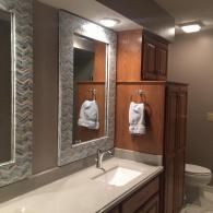 A bathroom vanity with dual mirrors, a white countertop, wooden cabinets, and a white towel hanging on a wall ring.