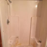 A white, single-piece fiberglass shower stall with visible staining and buildup in the basin and on the lower walls.