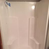 White acrylic shower stall with built-in corner seats and a showerhead on the left wall.