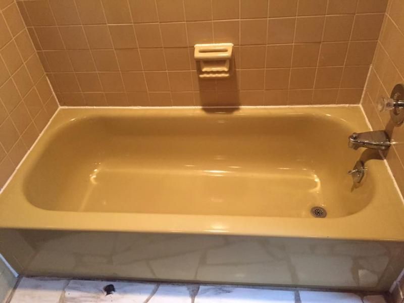 A beige bathtub and tiled wall with a soap dish, chrome faucet, and drain in a bathroom.