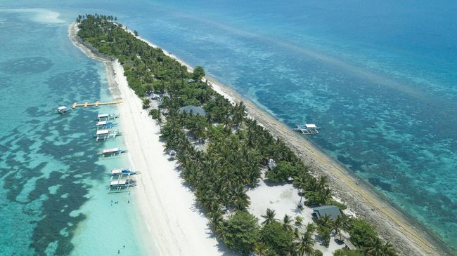 Un'isola stretta con palme, circondata da acque turchesi e barche.