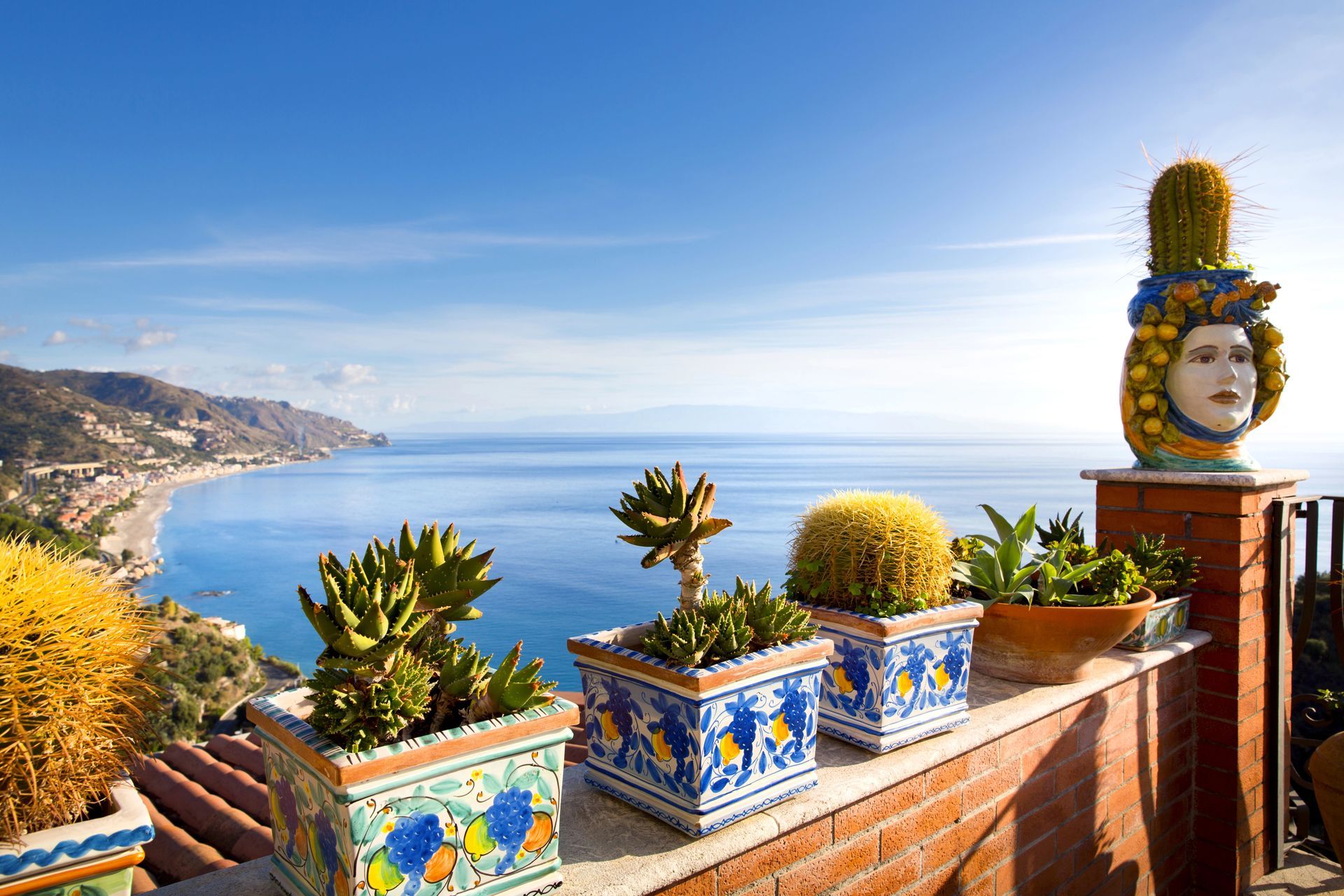 Terrazza con cactus in vaso e vista mare in Sicilia, Italia; cielo azzurro brillante.