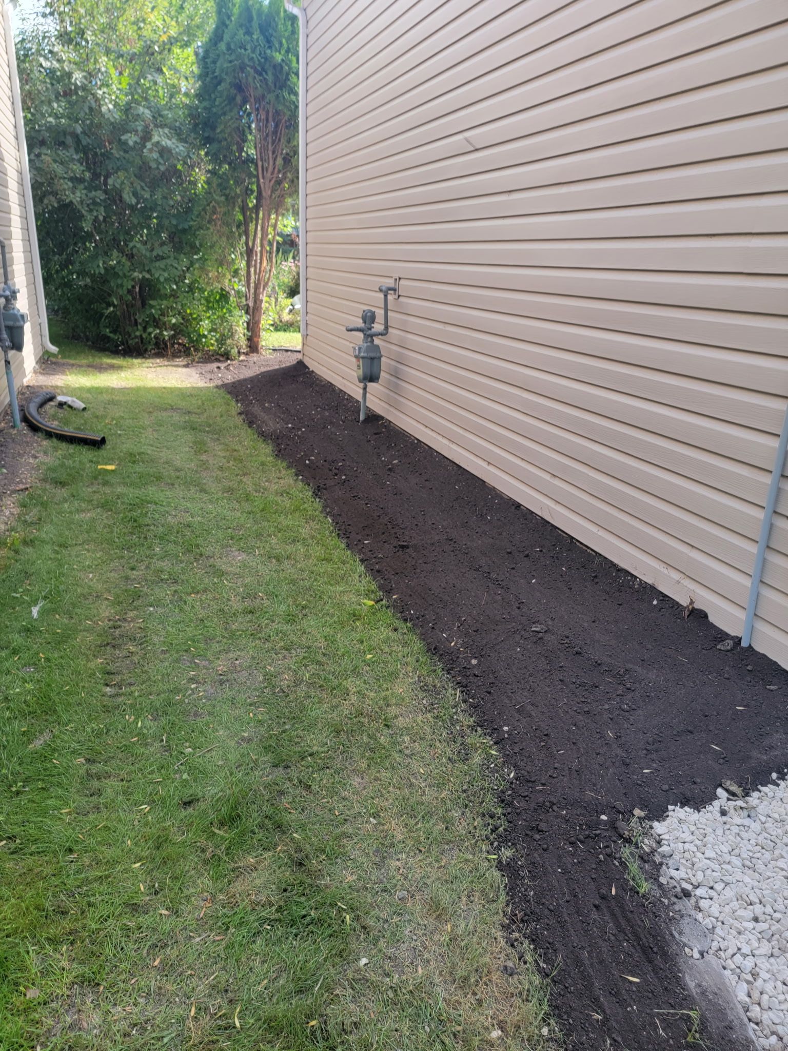 A view of a tan-sided house exterior with a freshly mulched garden bed along the wall and green grass in the yard.