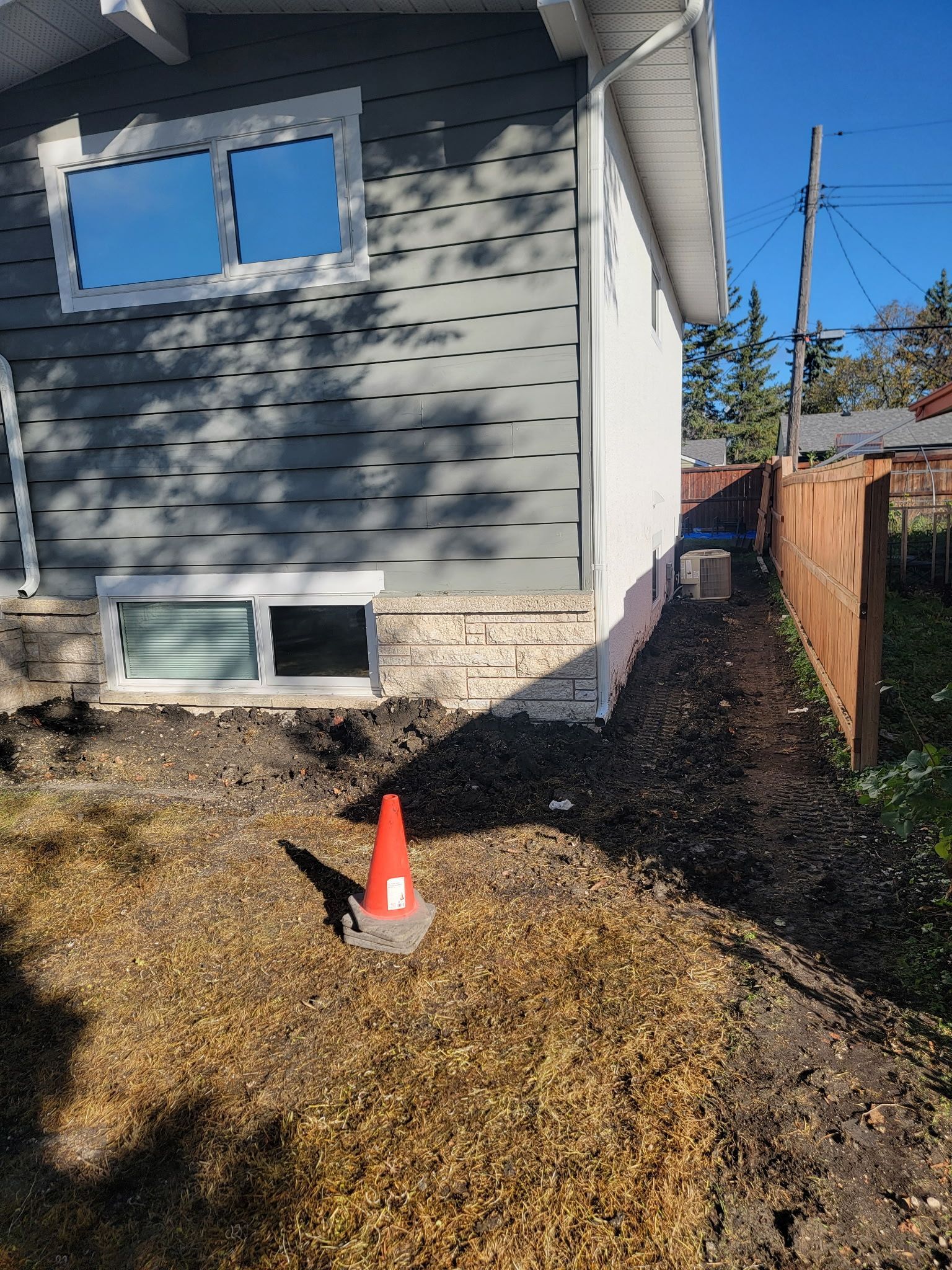 A residential house exterior with gray siding and brick foundation, featuring a small orange safety cone on the lawn.