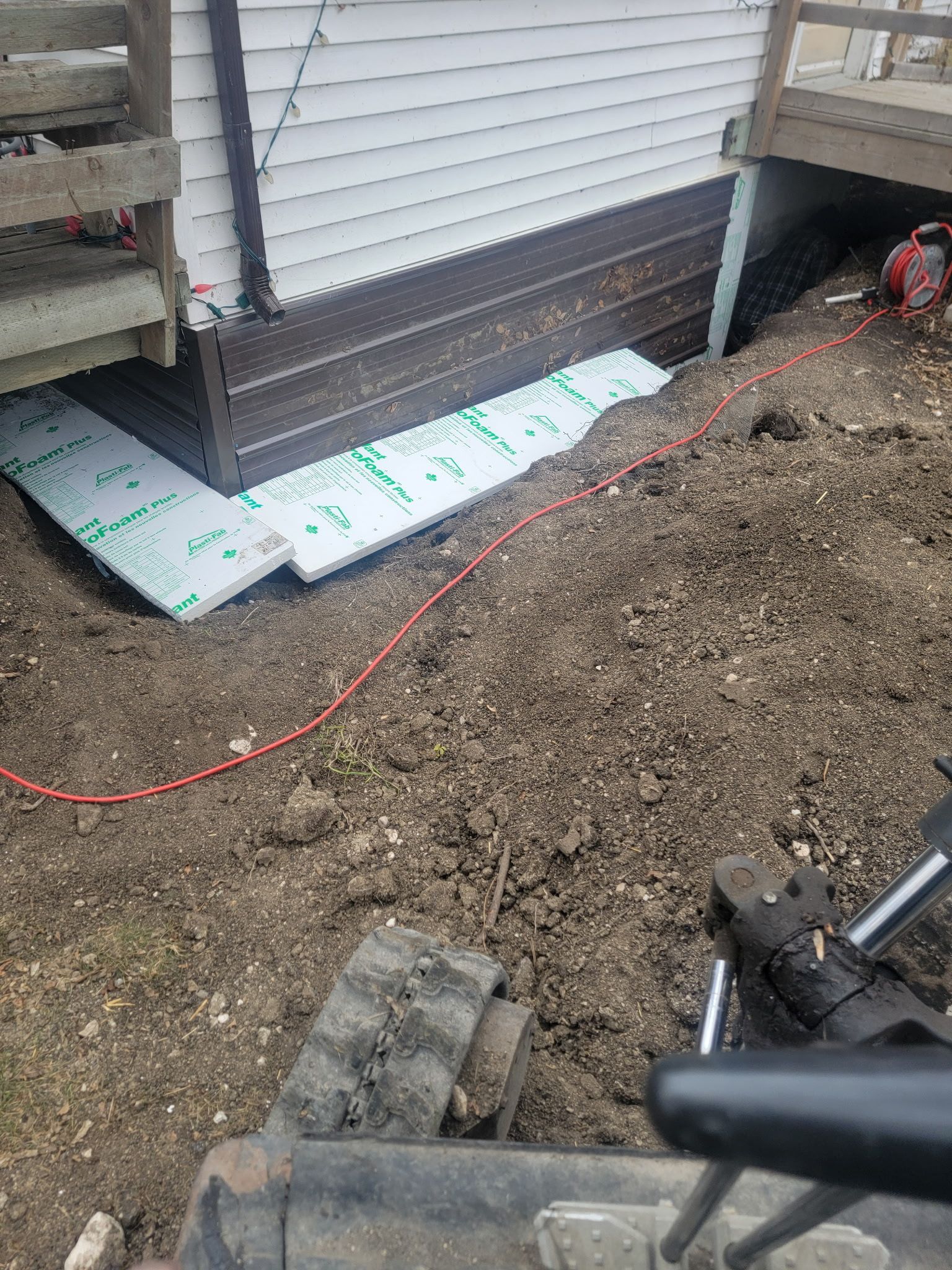 Foam insulation boards installed against a house foundation in a construction zone, viewed from an excavator cab.