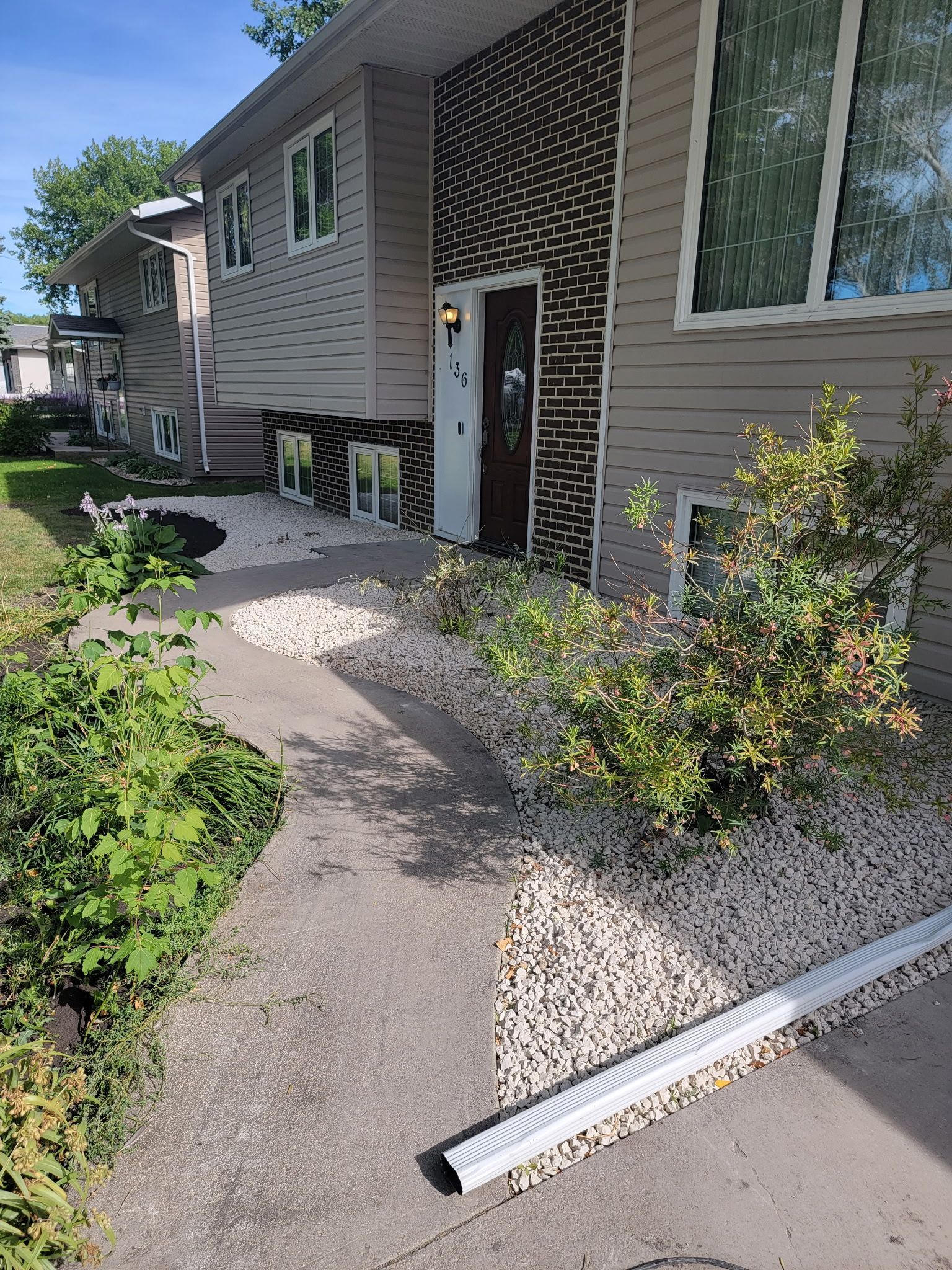 A tan house with a brown brick accent wall by the front door, featuring a concrete walkway and gravel landscaping.