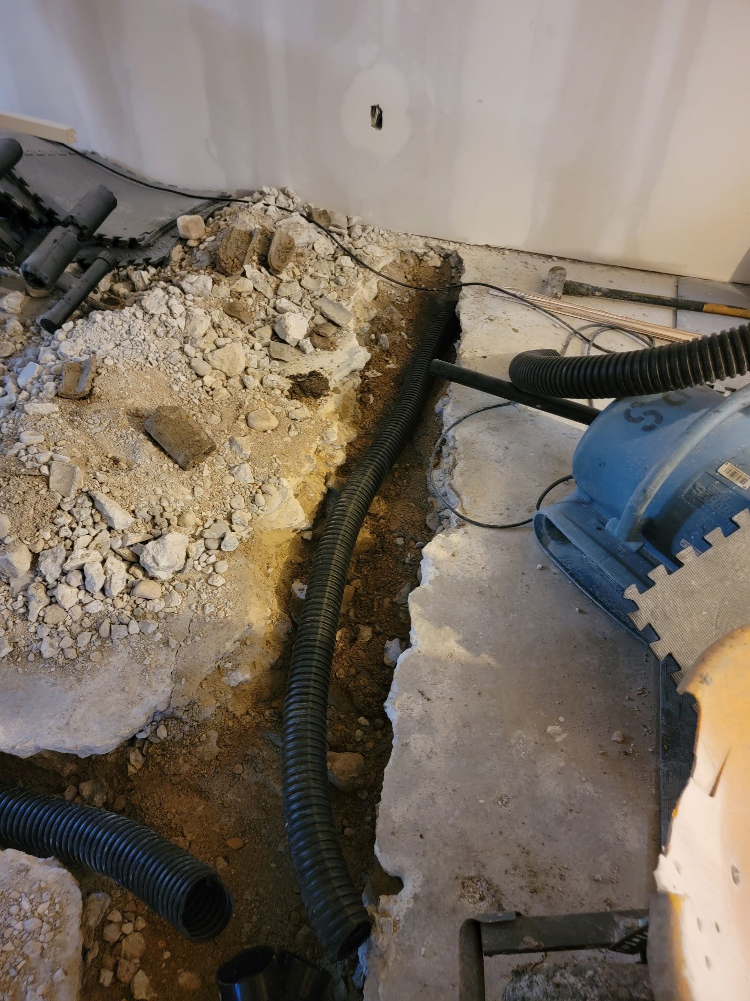 Black corrugated drainage pipe installed in a trench dug through a concrete basement floor.