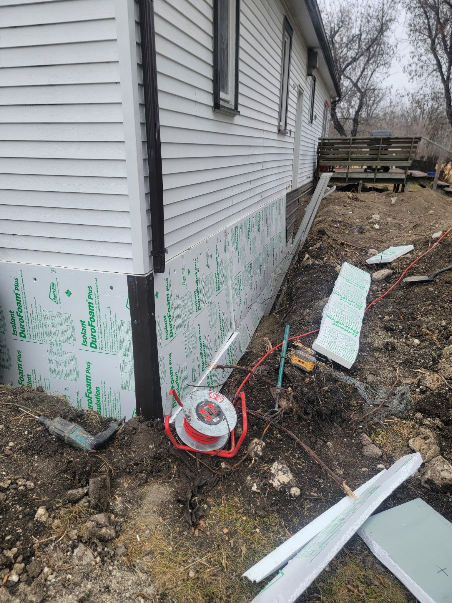White siding house exterior with foam insulation panels installed on the concrete foundation and construction tools nearby.