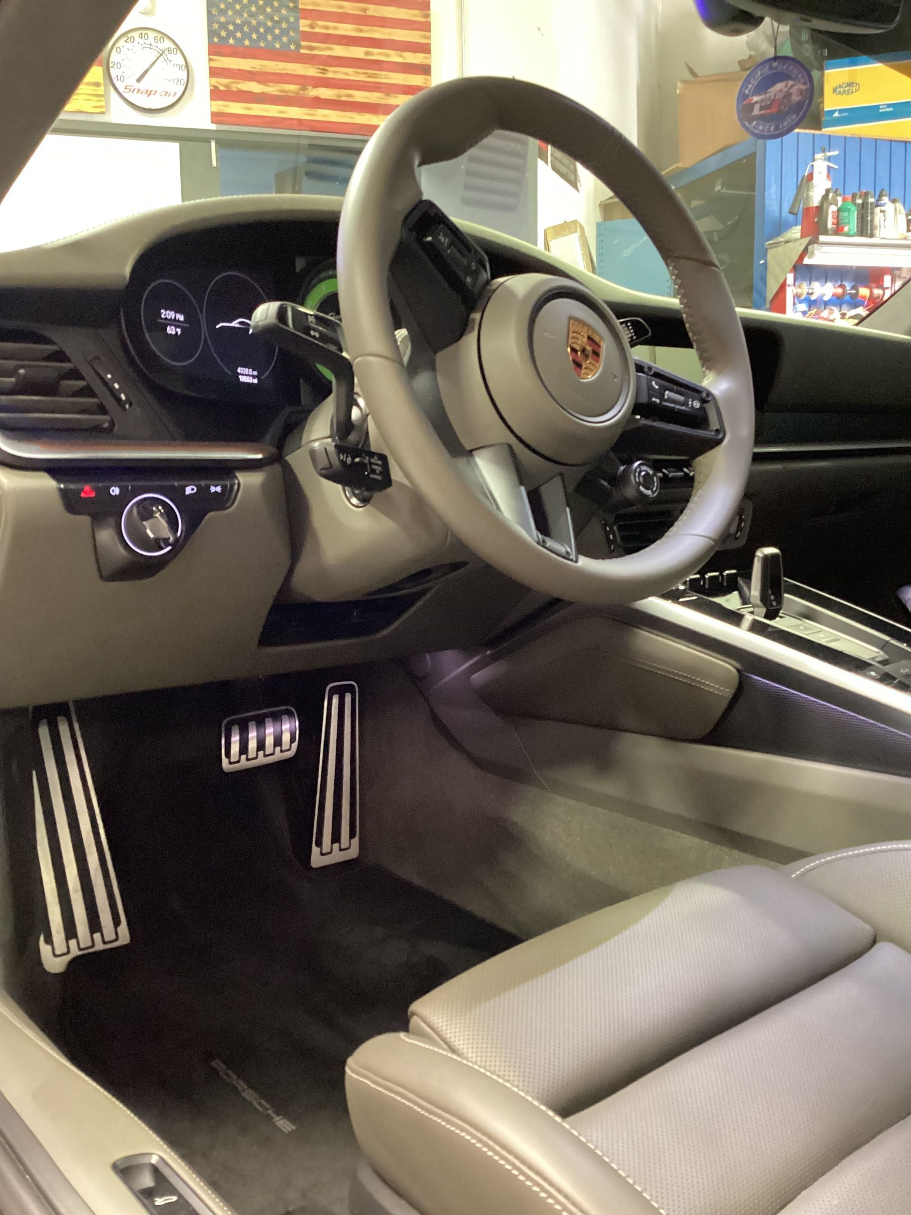 Interior of a Porsche sports car, featuring a gray leather interior, steering wheel, and metallic pedals.