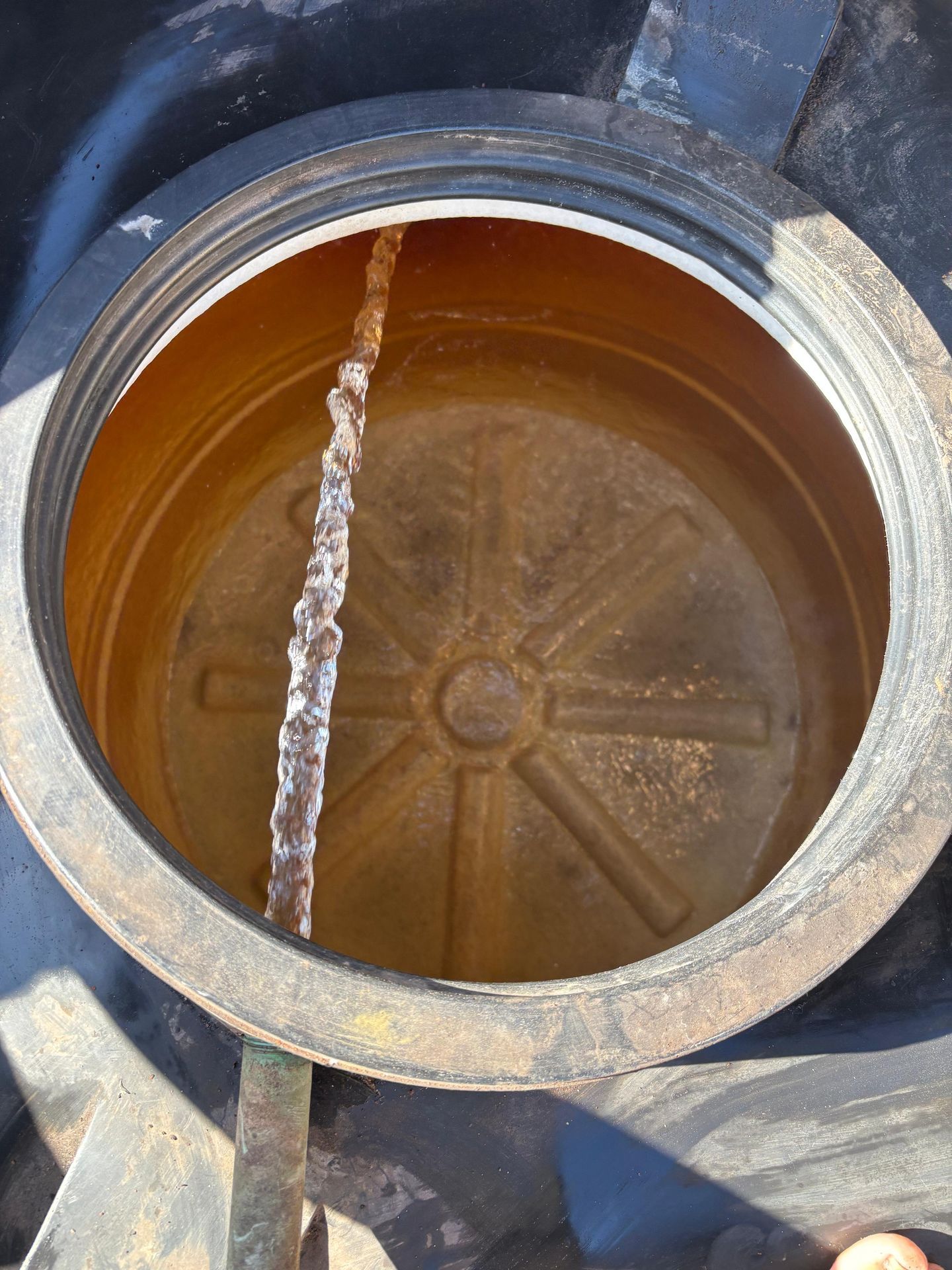 Dentro de un tanque negro, oxidado y abierto, cuelga una varilla de metal corroída.