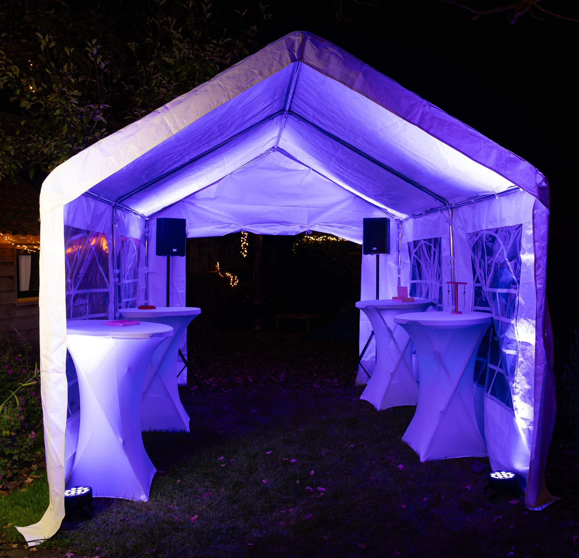 Feesttent met witte tafels en paarse verlichting in de avond.