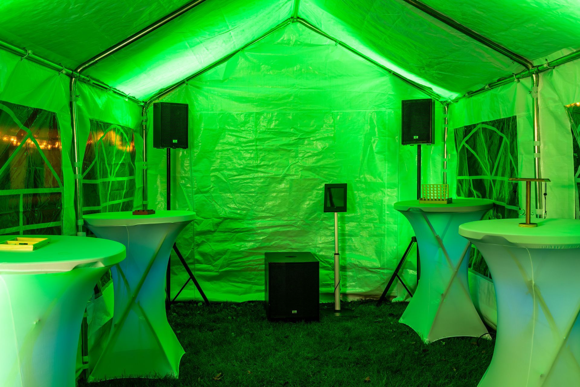 Felgroen licht vult een tent met hoge tafels en audioapparatuur, waaronder luidsprekers en een subwoofer.