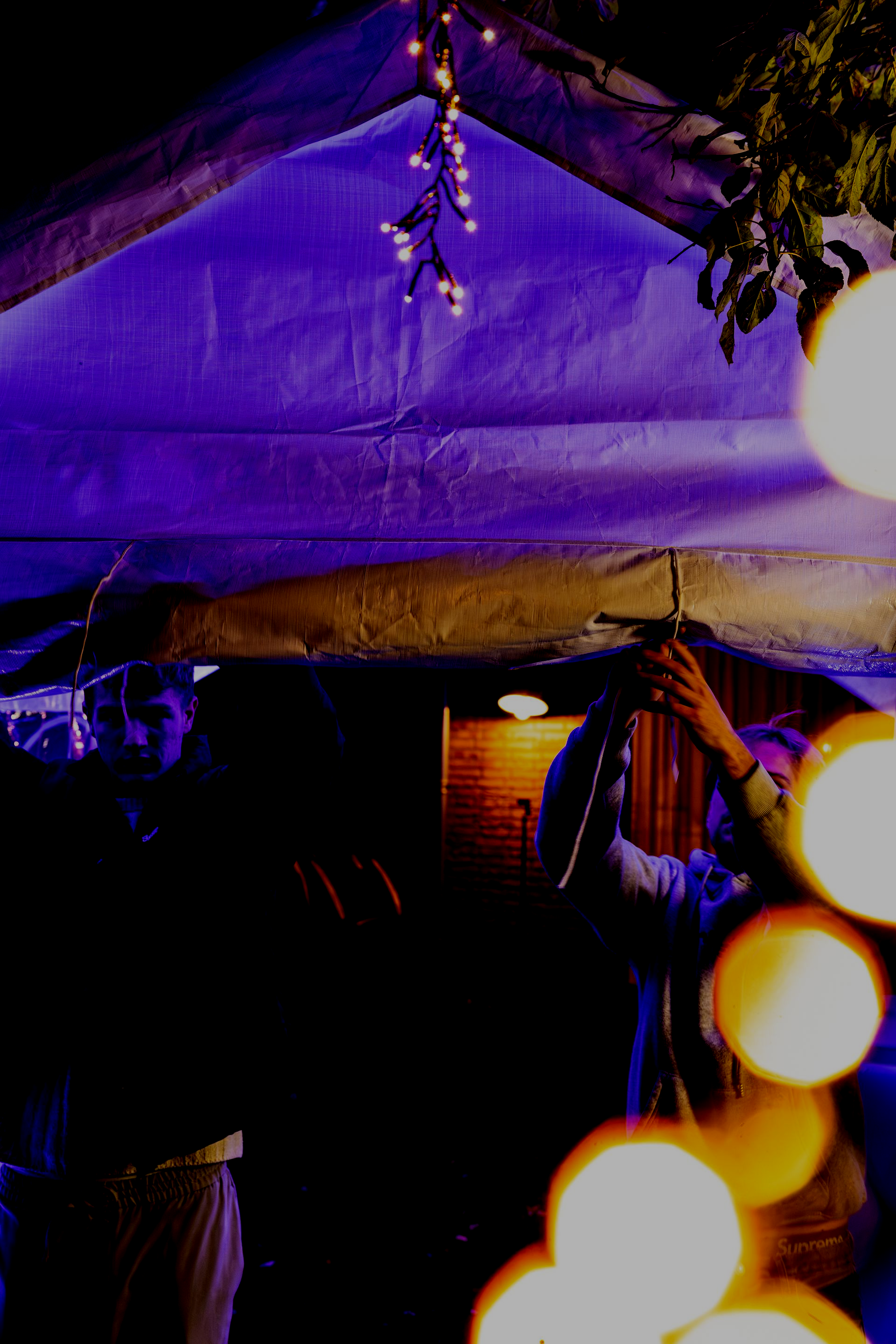 Iemand zet een frame op onder een tentdoek dat 's nachts verlicht wordt door lichtsnoeren.