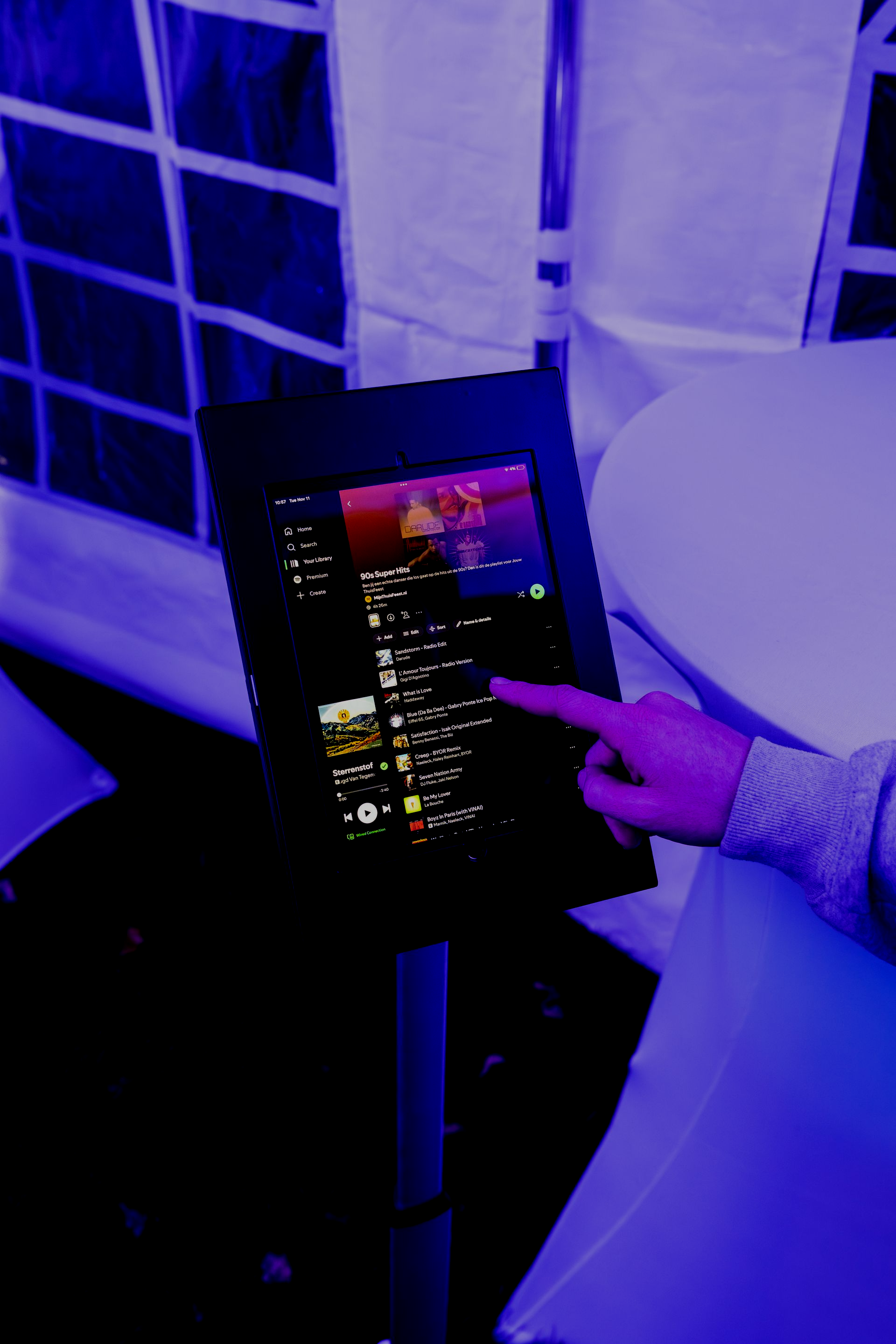 Iemand selecteert met zijn vinger een nummer op een tabletscherm dat op een standaard staat in een schemerig verlichte, blauwgetinte ruimte.