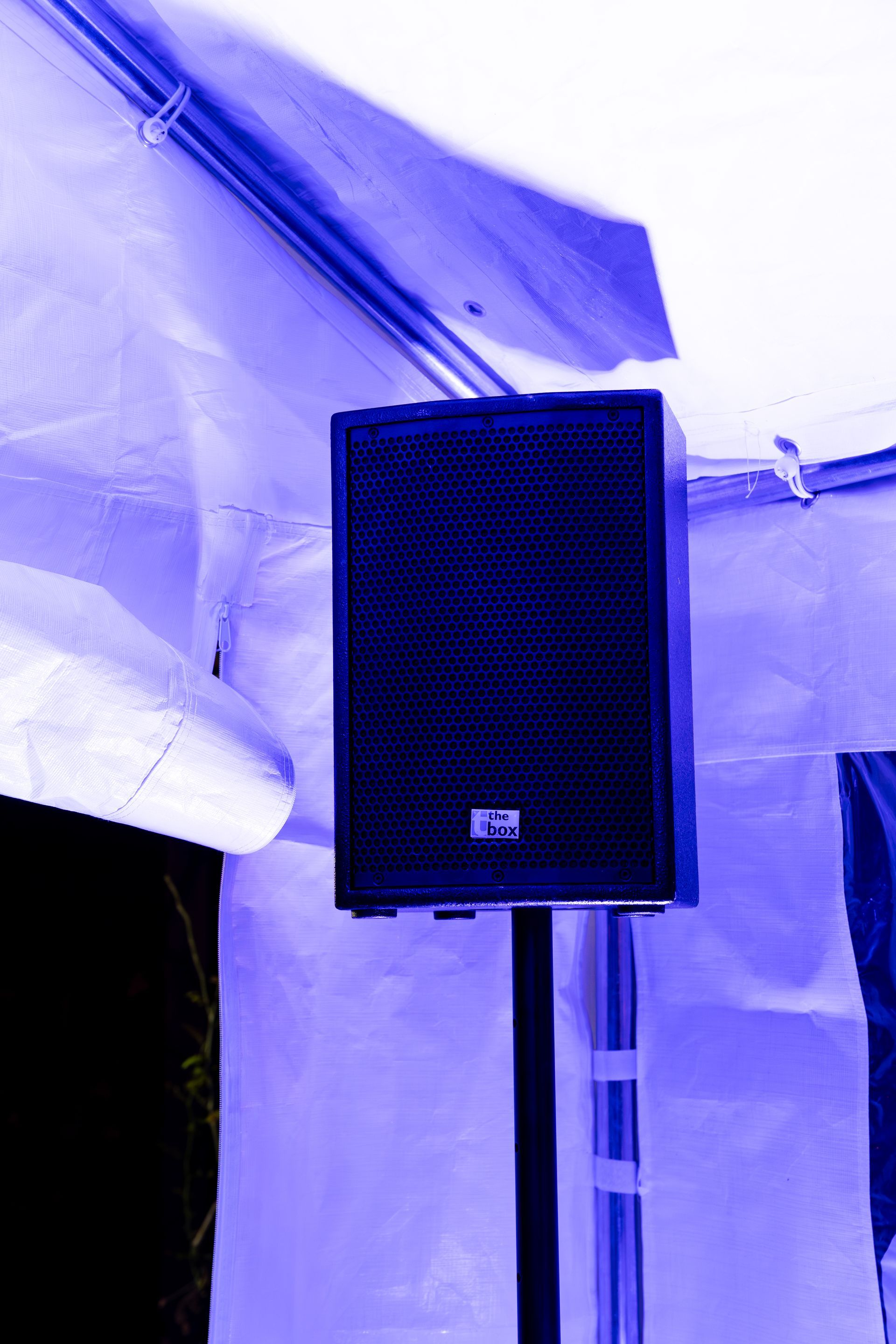 Een zwarte luidspreker, gemonteerd op een standaard in een witte tent die verlicht wordt door blauw licht.