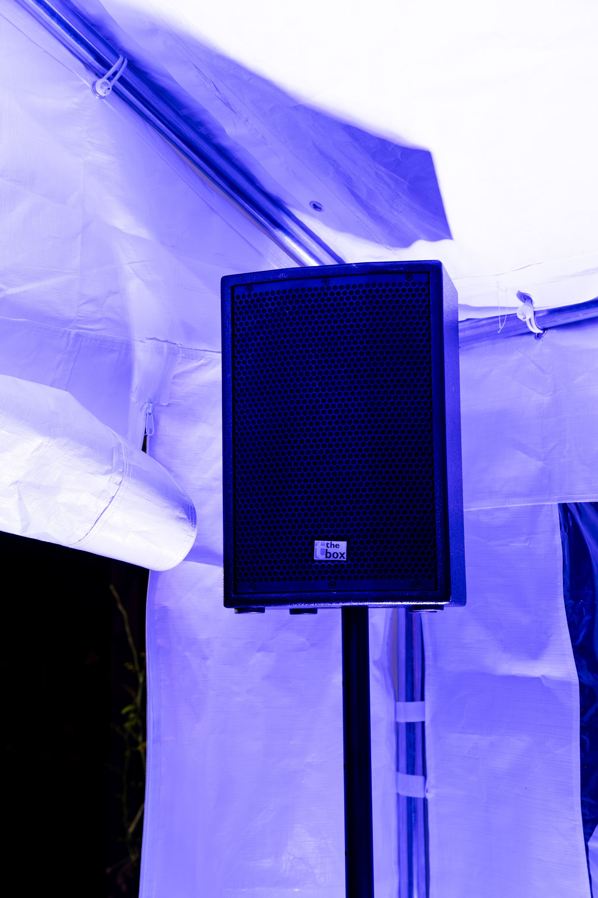 Een zwarte luidspreker, gemonteerd op een standaard in een witte tent, wordt verlicht door paars licht.