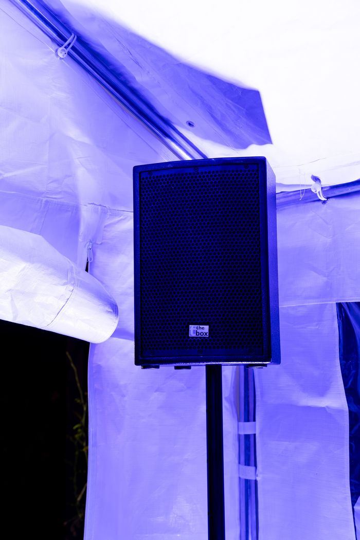 Een zwarte luidspreker, gemonteerd op een standaard in een witte tent die verlicht wordt door blauw licht.
