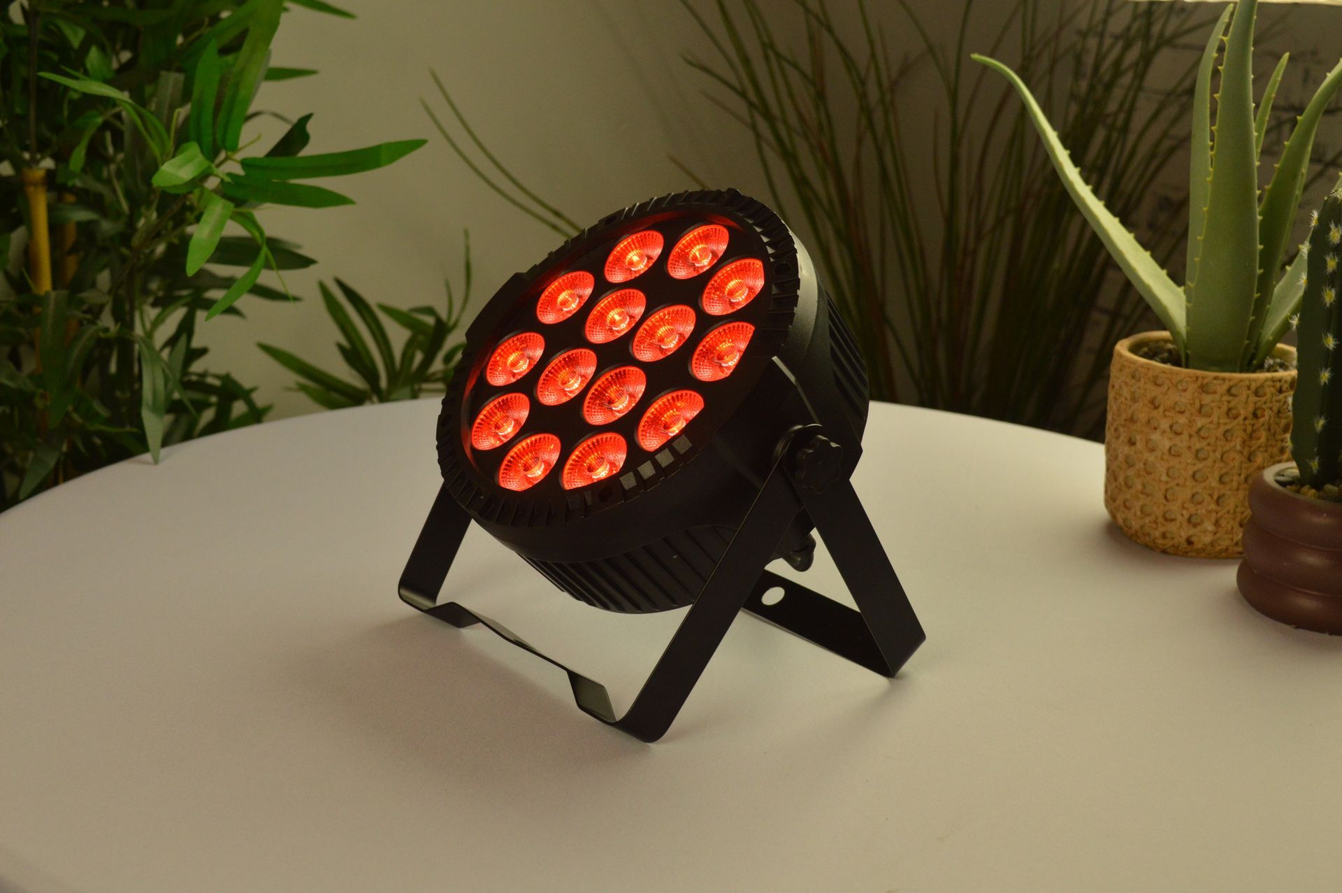 Een rode LED-podiumlamp staat op een witte tafel naast potplanten.