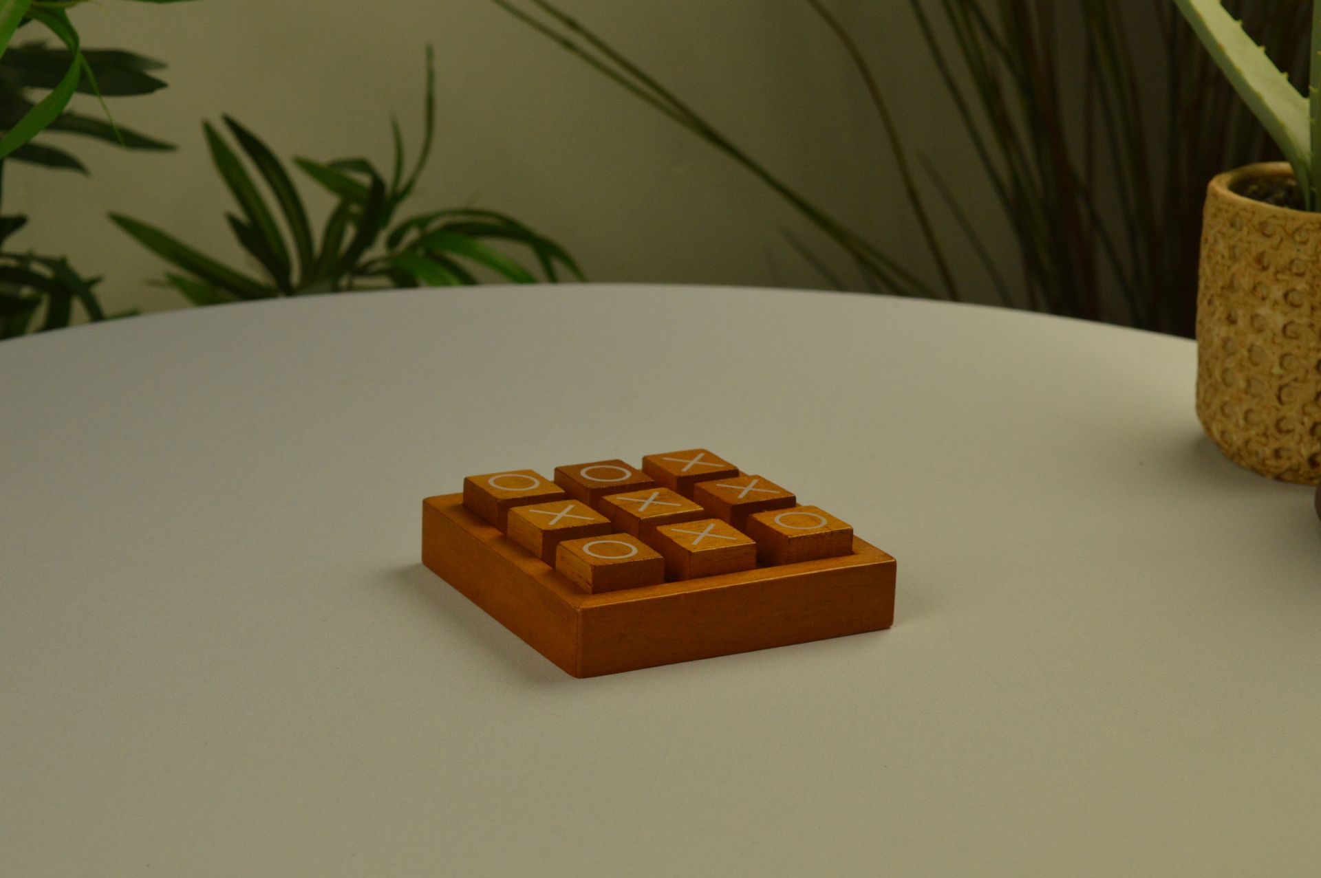 Een houten ringwerpspel met twee hangende ringen op een standaard staat op een witte tafel naast kamerplanten.