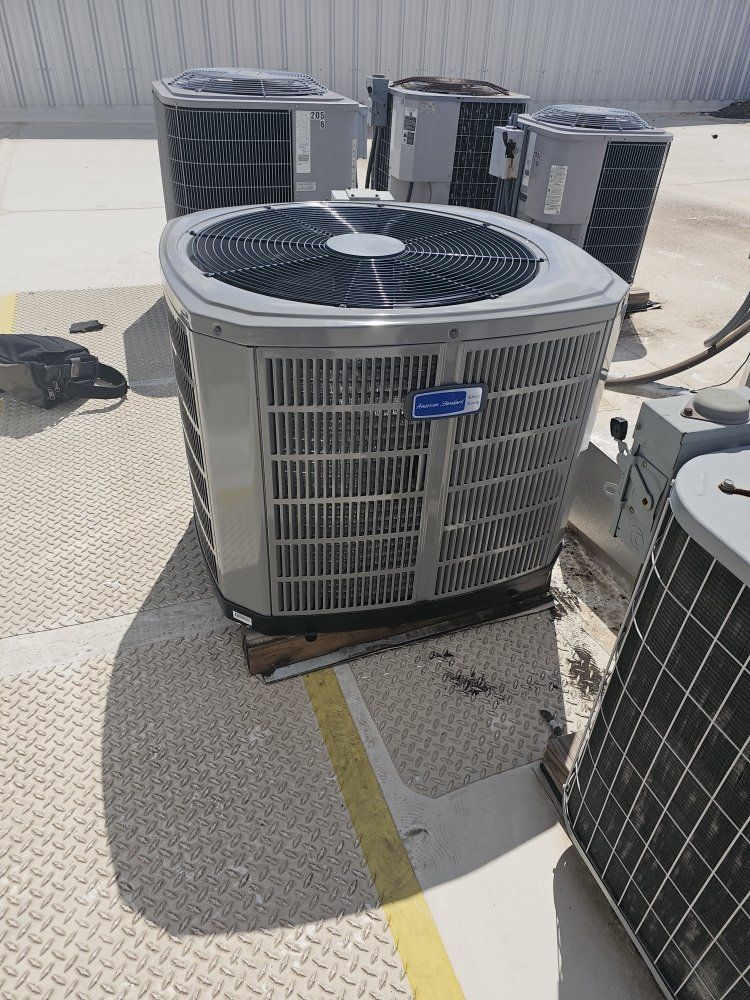 Multiple air conditioning units on a rooftop, the closest unit is centered and gray with a black fan.