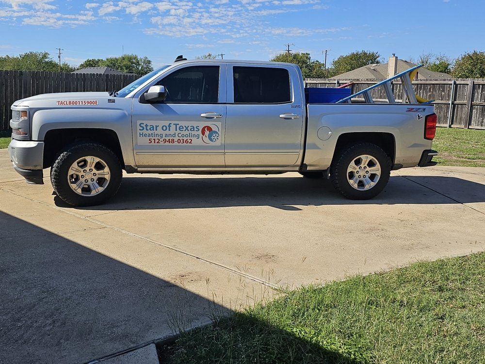 Silver pickup truck parked on concrete driveway; it has a company logo on the side and a ladder in the bed.