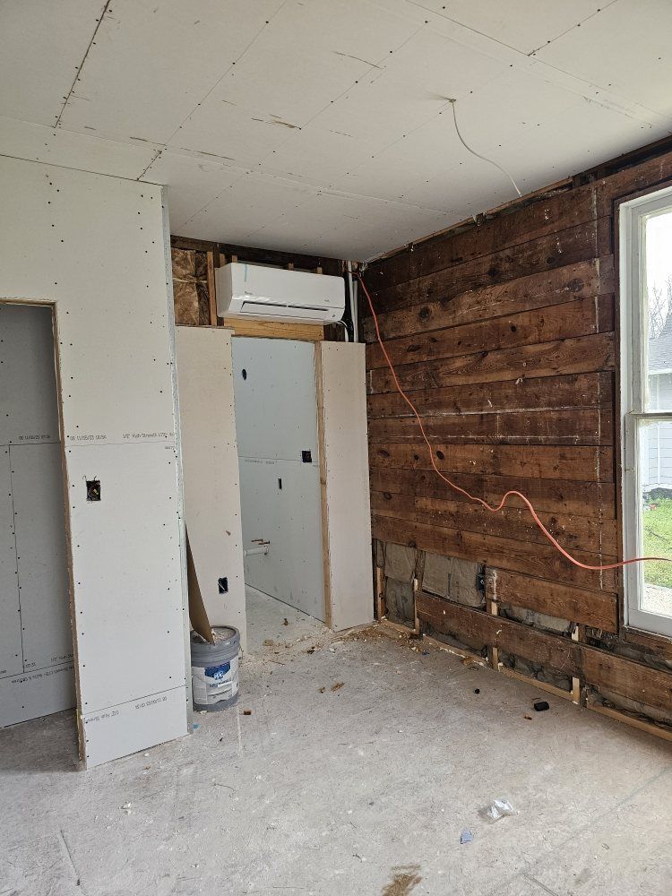 Room under construction with exposed wood wall, drywall, and an air conditioning unit. A window is visible on the right.