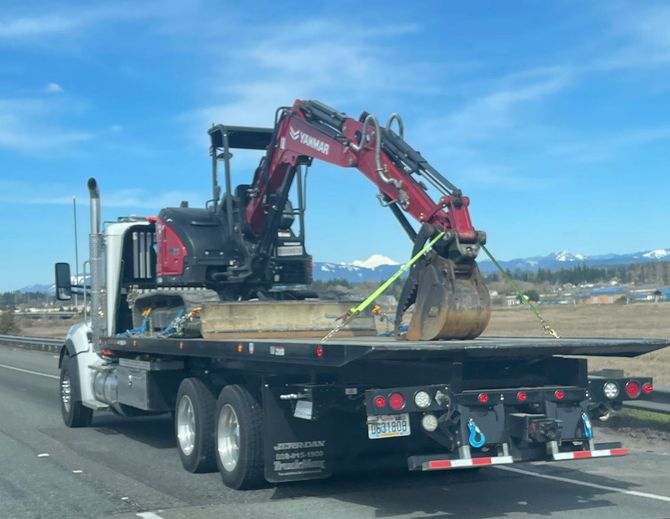 A tow truck is carrying an excavator on the back of it.