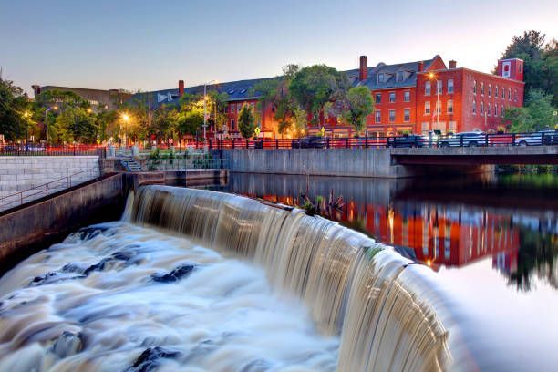 A waterfall in the middle of a river with a bridge in the background.