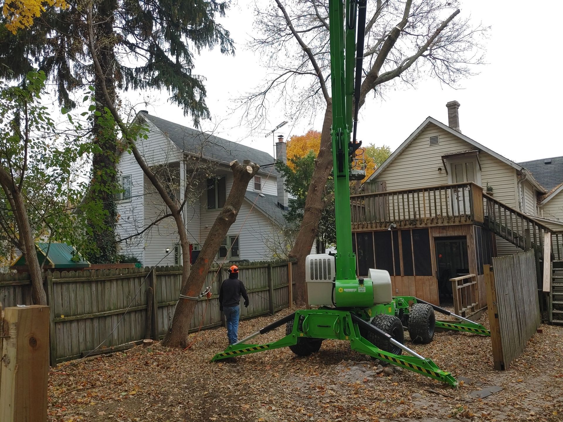 A man is standing in front of a green crane in a backyard.