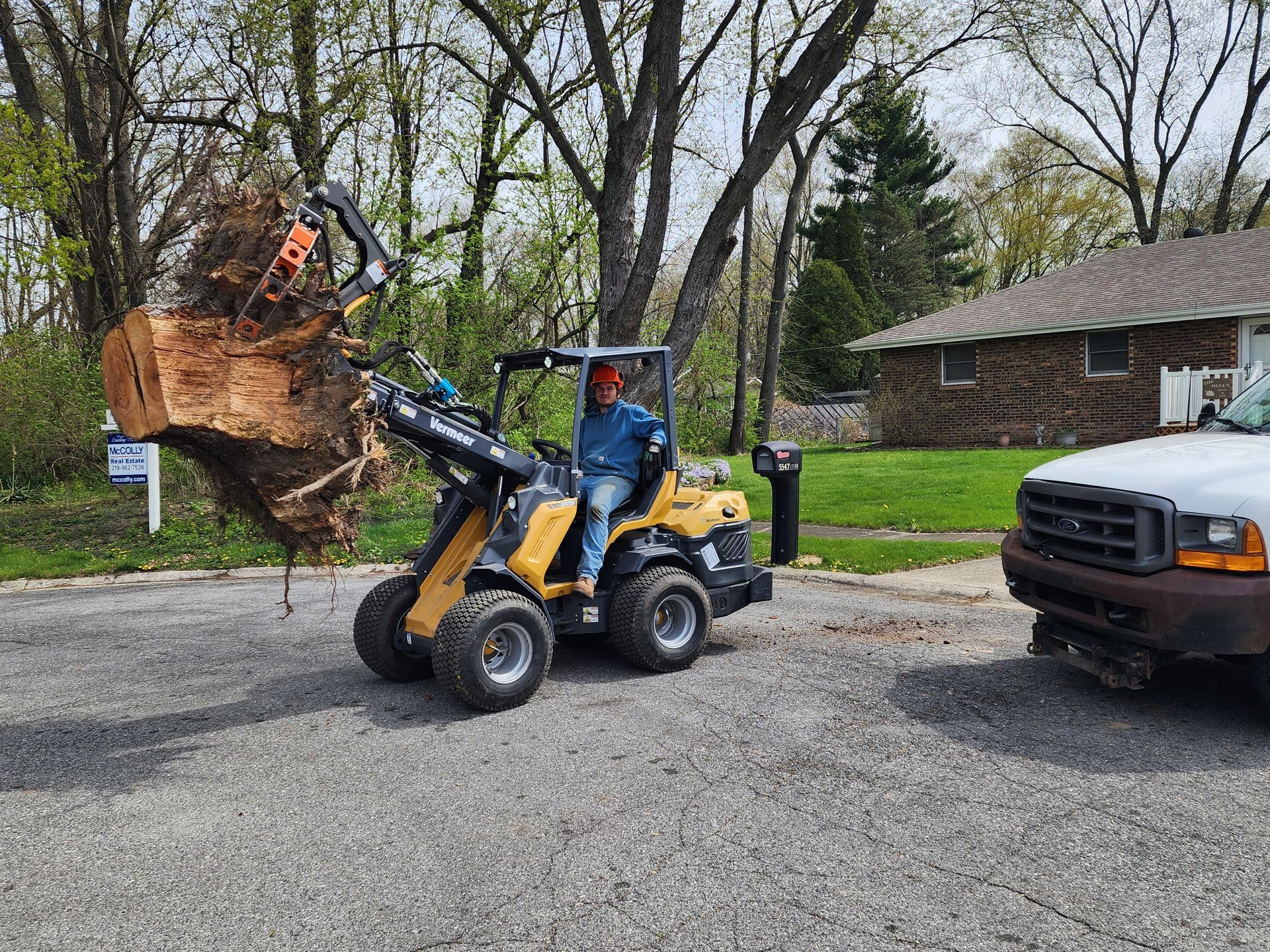 A man is driving a tractor with a tree stump in the back.