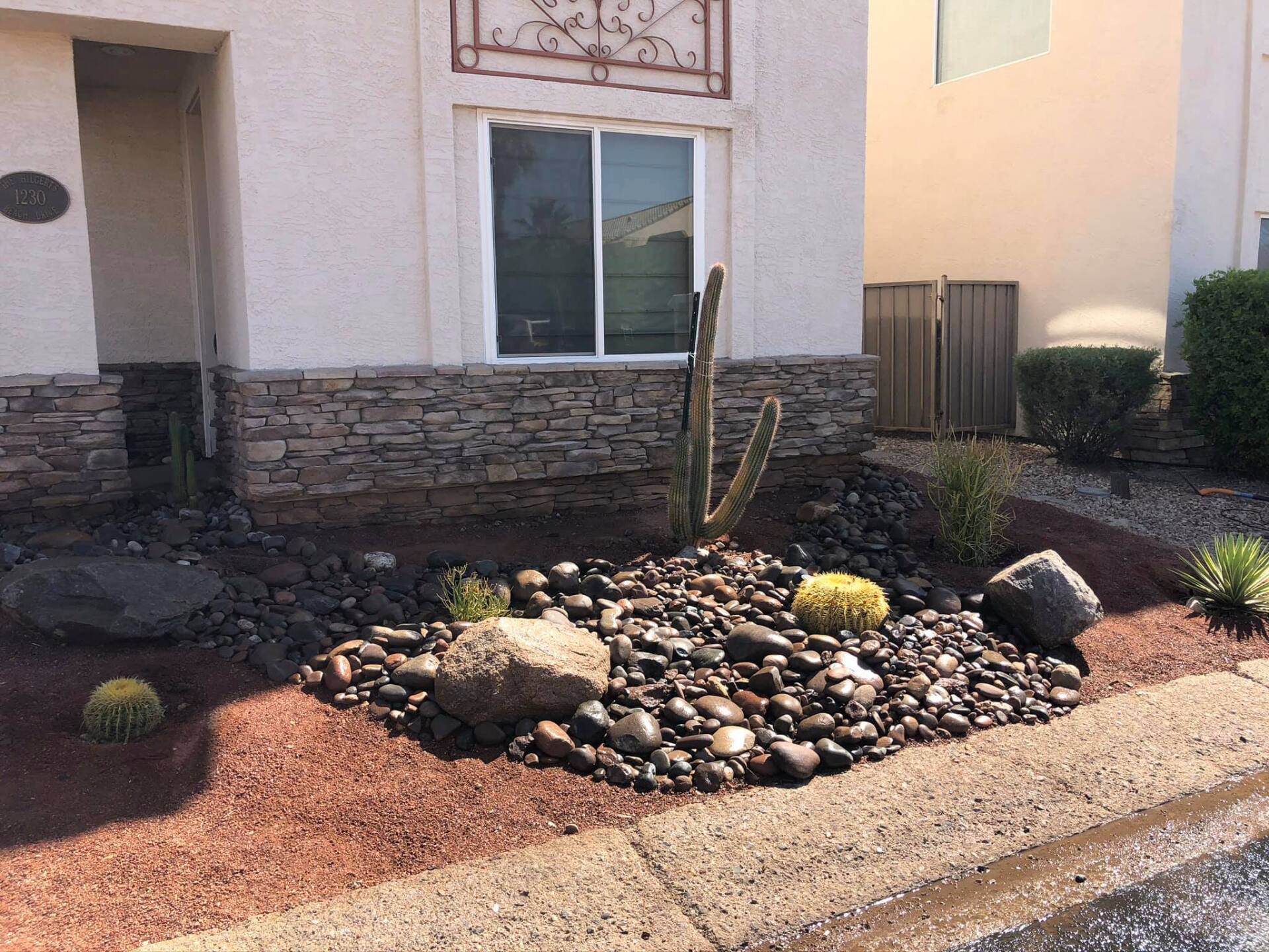 A cactus is growing in a rock garden in front of a house.