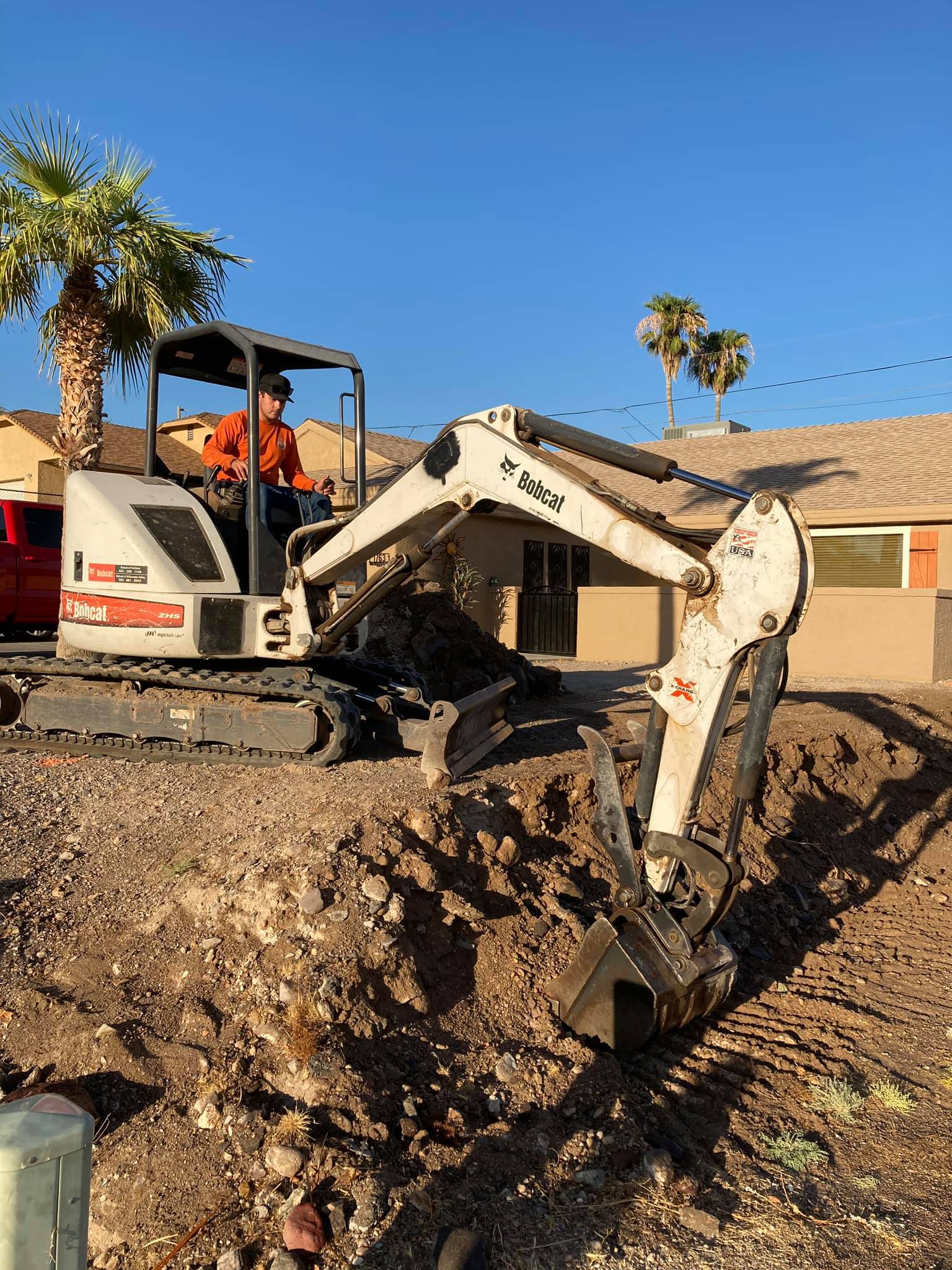A man is driving a small excavator in a dirt field.