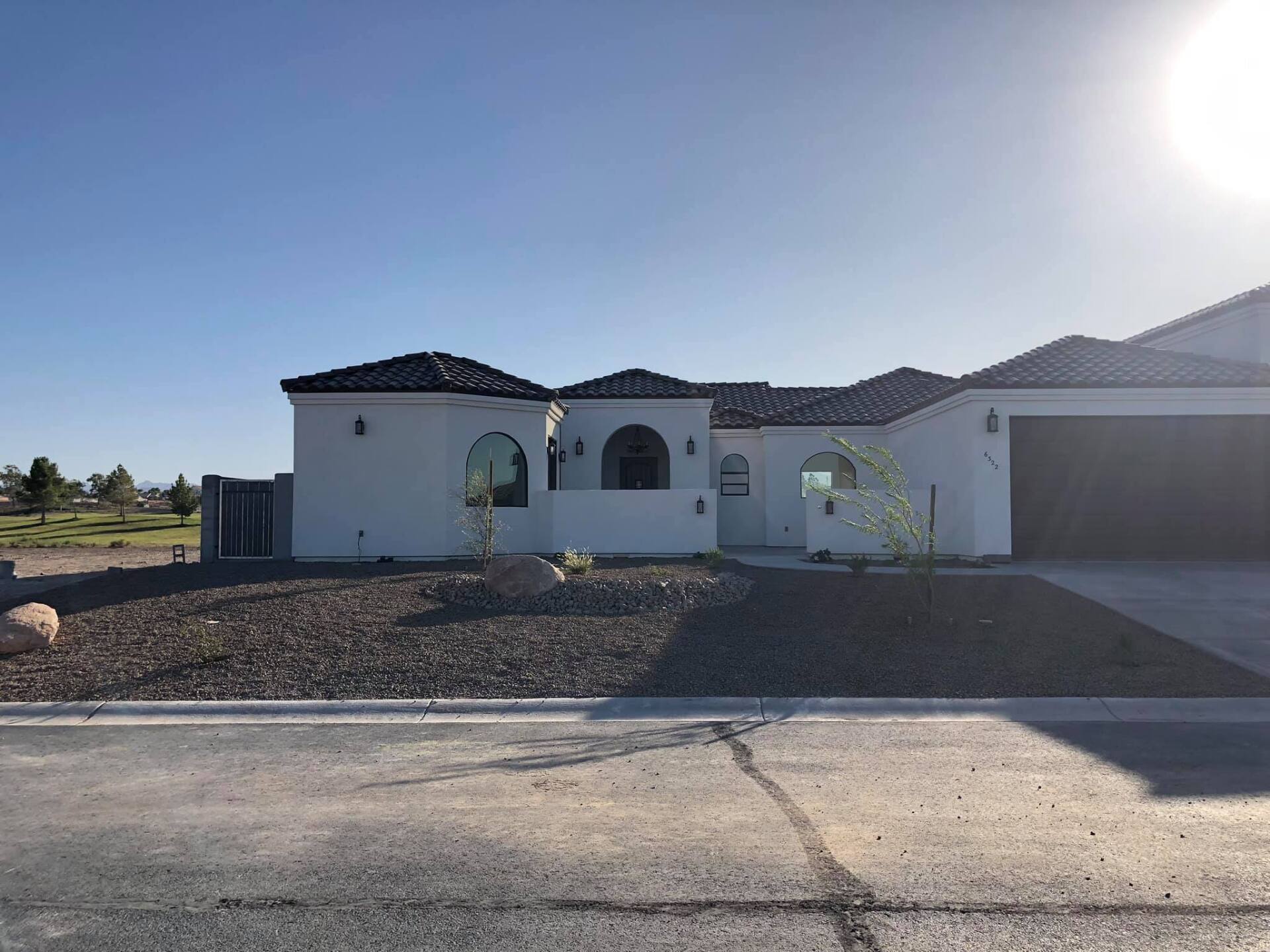 A white house with a black roof is sitting on top of a dirt field.