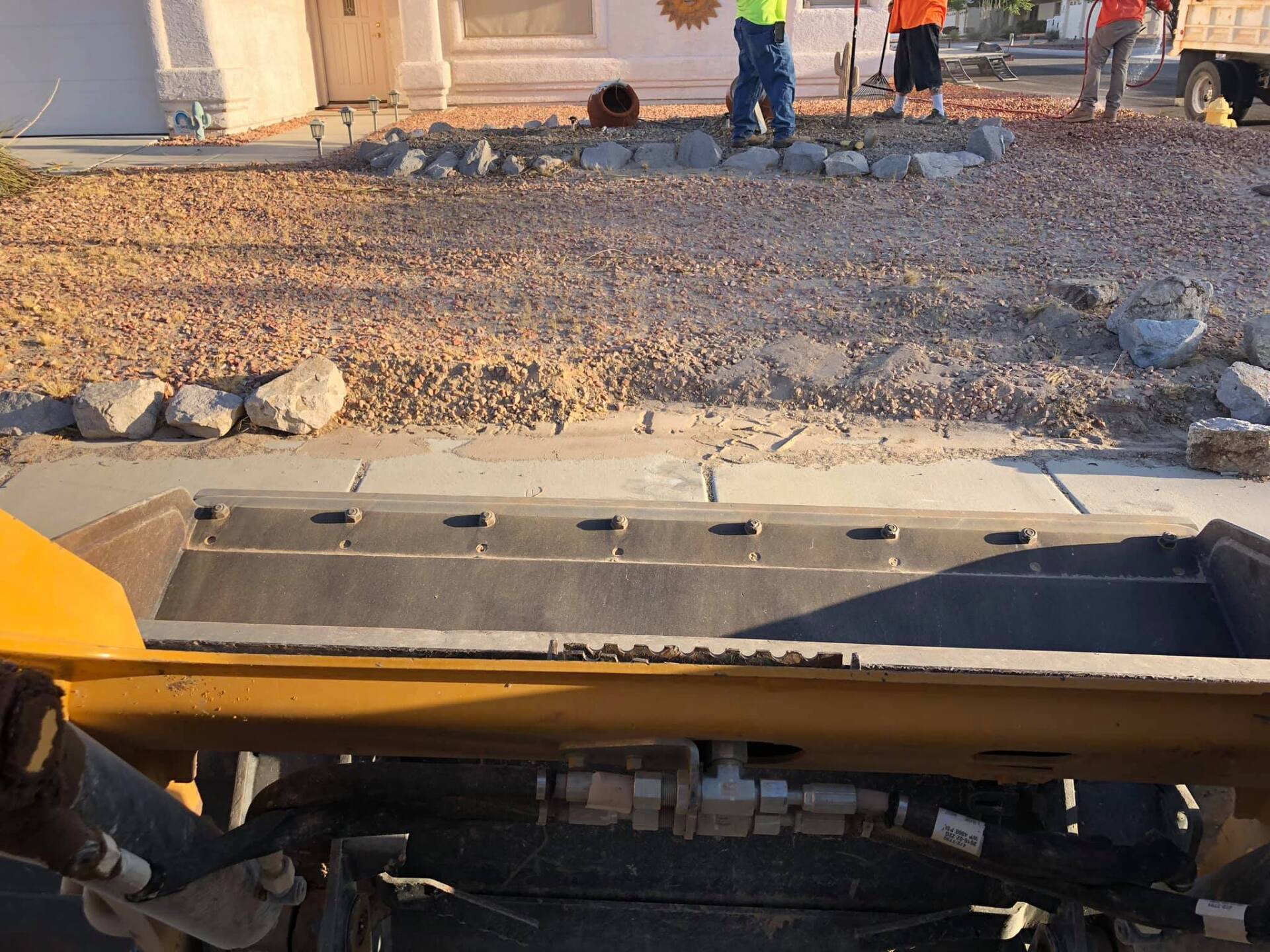 A group of construction workers are working on a driveway in front of a house.