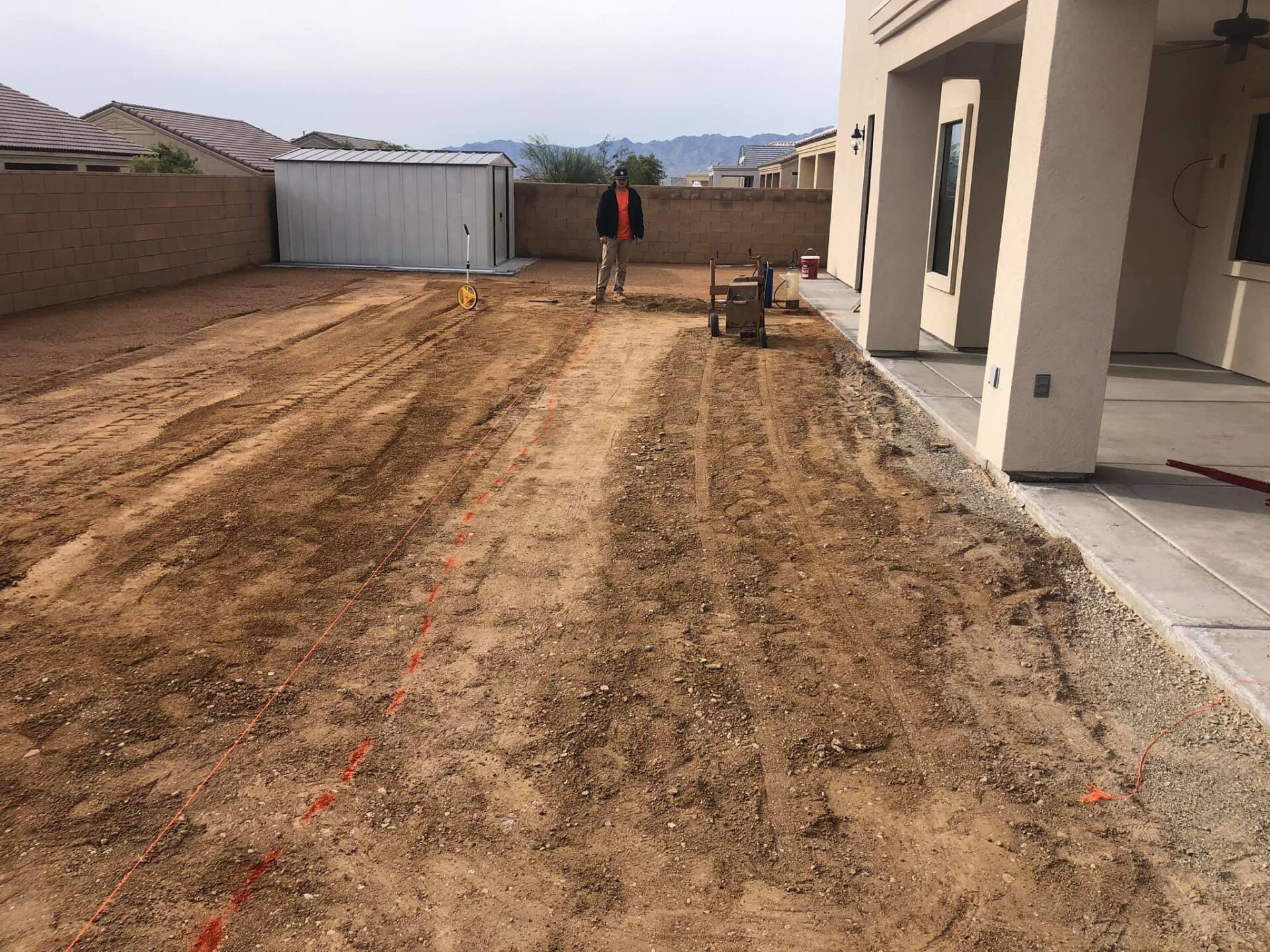 A man is standing in a dirt field in front of a house.