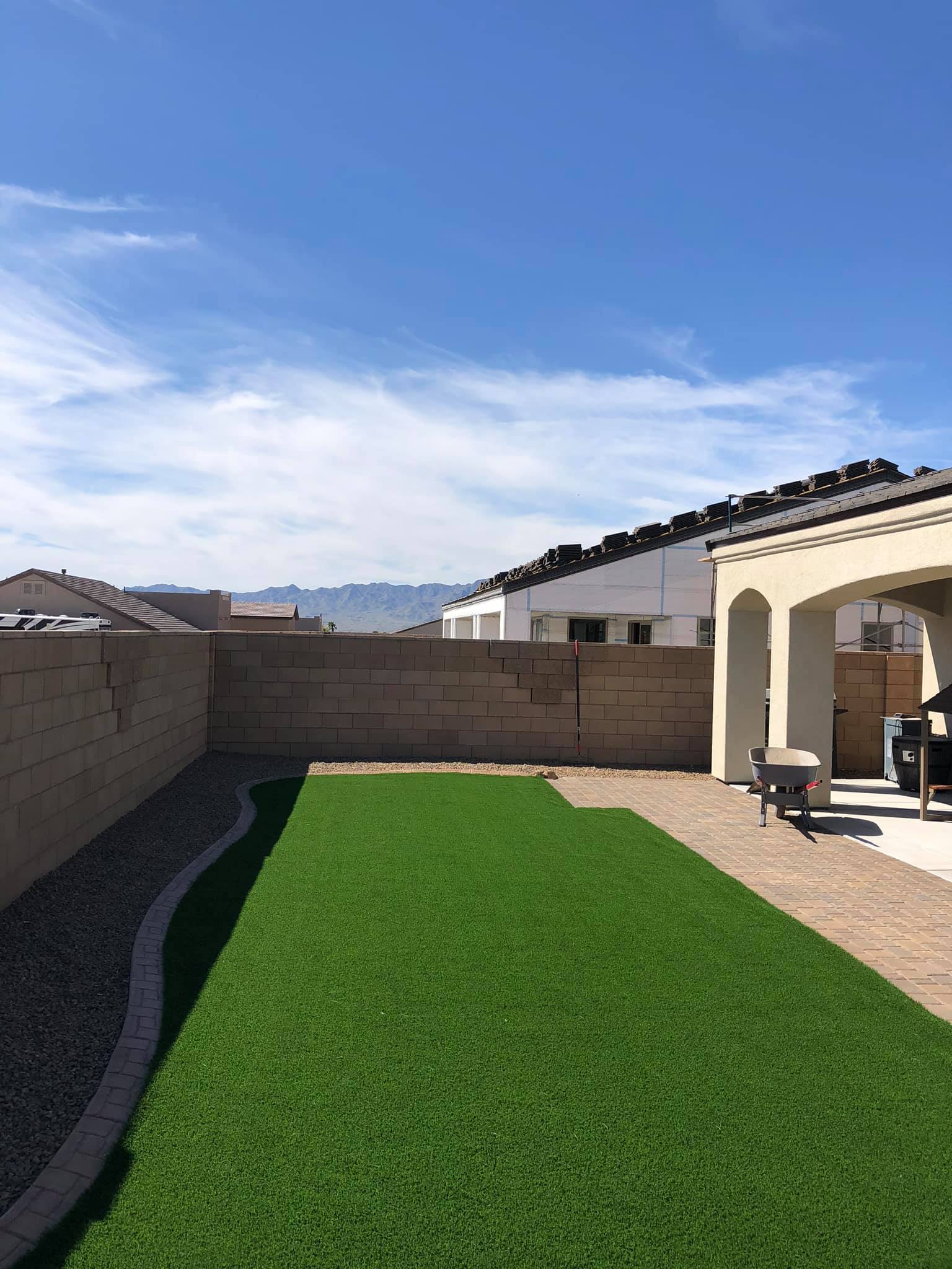 A backyard with a lush green lawn and a brick wall.