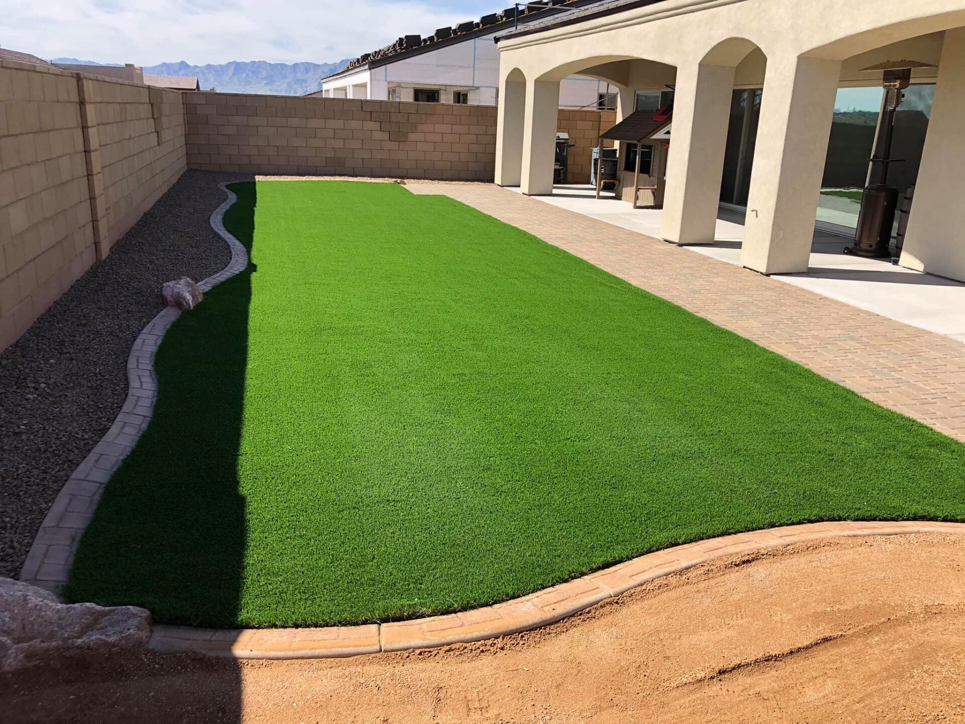 A backyard with a lush green lawn and a brick wall.