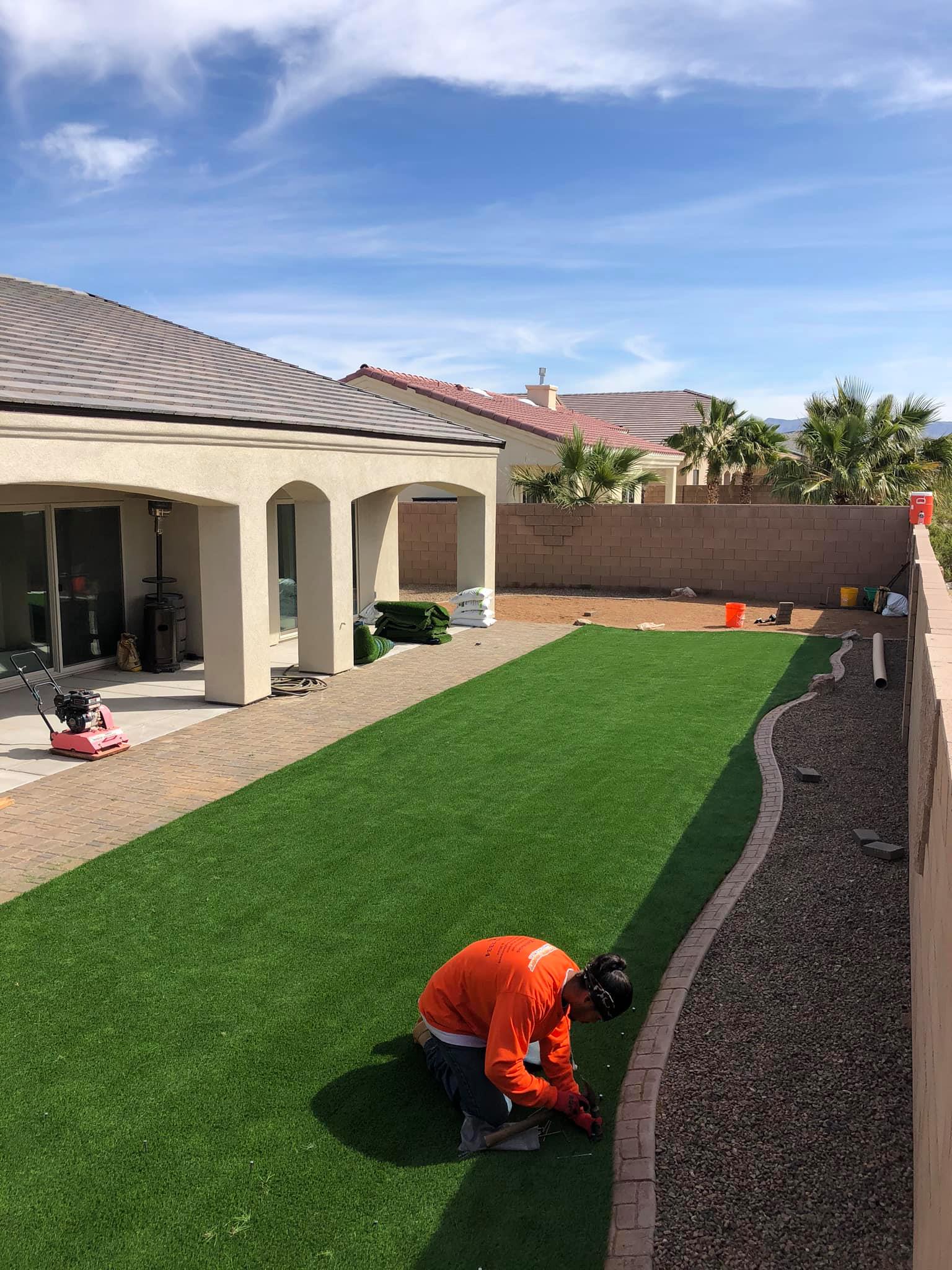 A man is kneeling on the grass in a backyard.