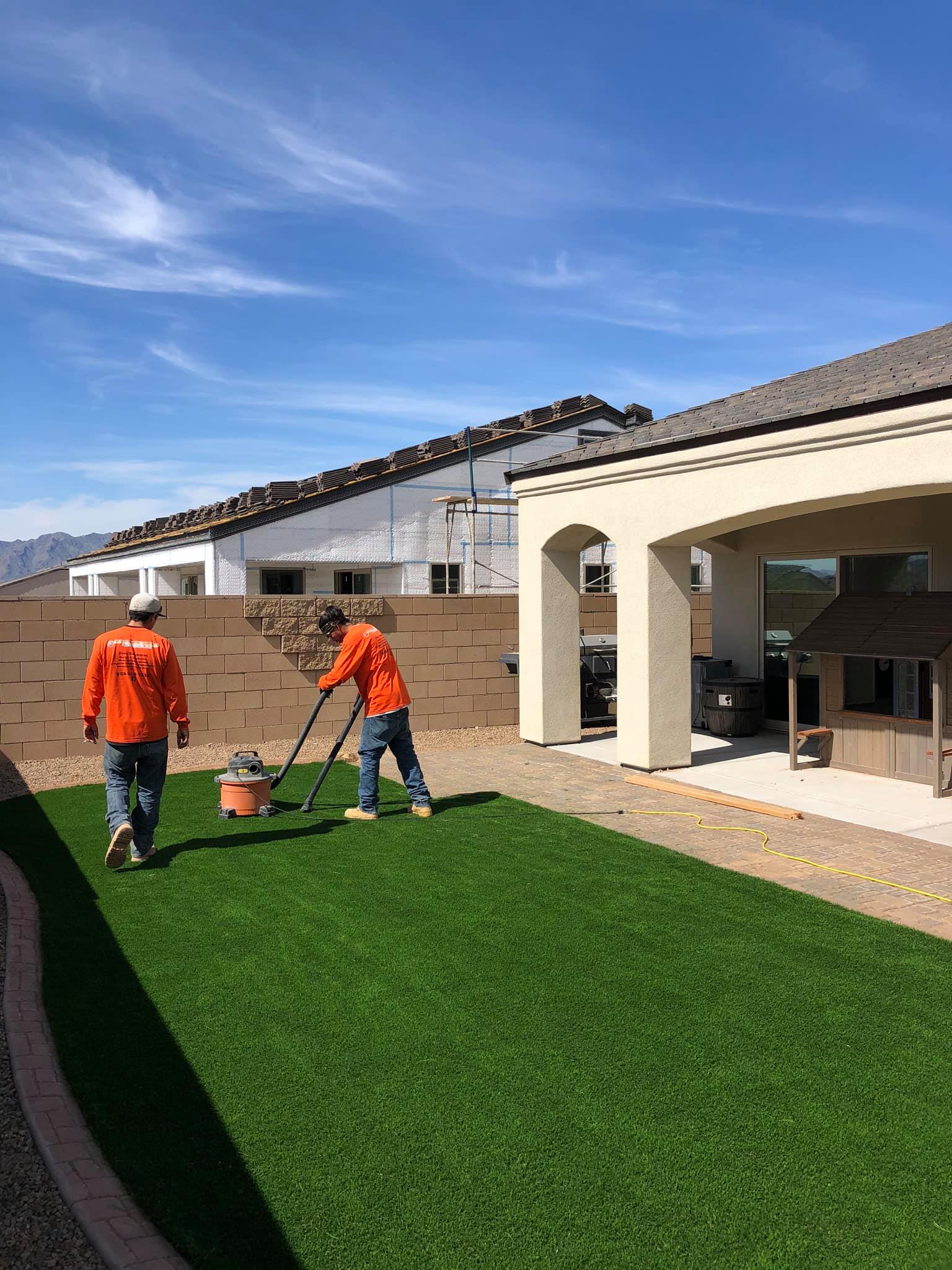 Two men are mowing a lush green lawn in front of a house.