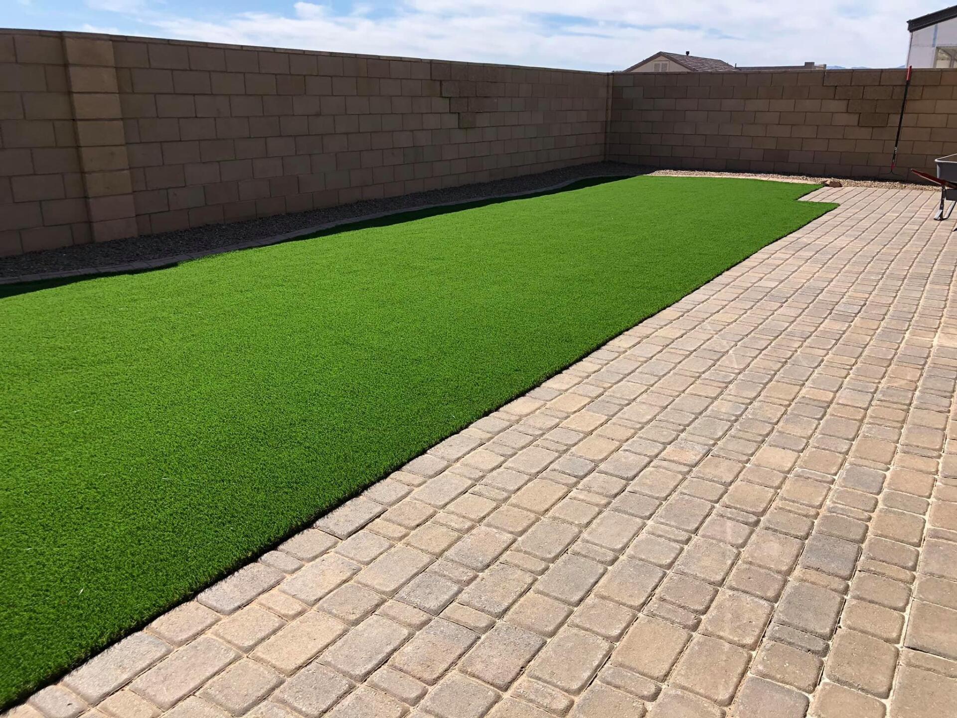 A backyard with a brick walkway and a lush green lawn.