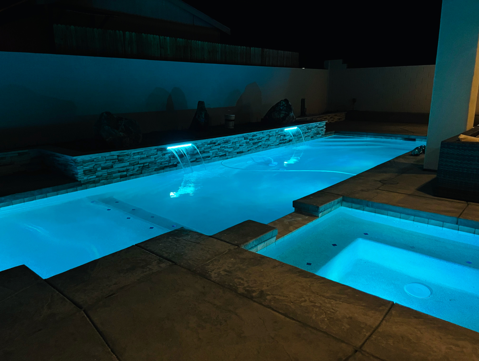 A large swimming pool is lit up at night with blue lights.